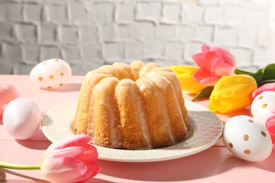 Photo of Delicious bundt cake, Easter eggs and tulips on pink wooden table, closeup