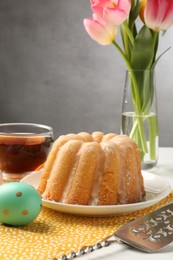 Photo of Delicious bundt cake, Easter egg, tea and tulips on table