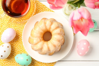 Photo of Delicious bundt cake, Easter eggs, tea and tulips on white wooden table, flat lay