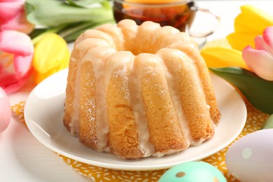 Photo of Delicious bundt cake, Easter eggs, tea and tulips on white wooden table, closeup