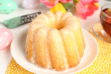 Photo of Delicious bundt cake, Easter eggs, tea and tulips on table, closeup