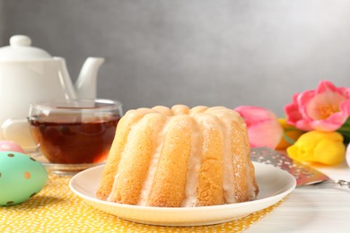 Photo of Delicious bundt cake, Easter eggs, tea and tulips on white wooden table, closeup