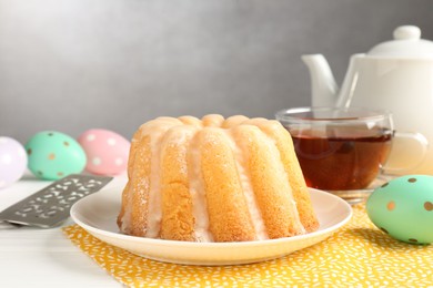 Photo of Delicious bundt cake, Easter eggs, tea and server on white wooden table, closeup