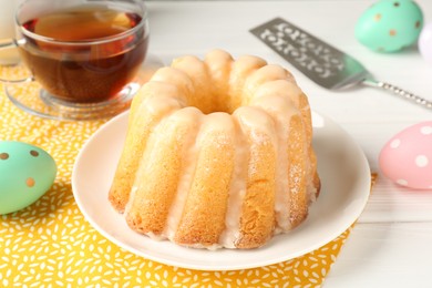 Photo of Delicious bundt cake, Easter eggs, tea and server on white wooden table, closeup