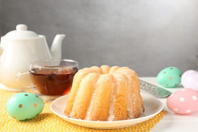 Photo of Delicious bundt cake, Easter eggs and tea on white wooden table, closeup