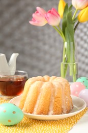 Photo of Delicious bundt cake, Easter eggs, tulips and tea on table, closeup