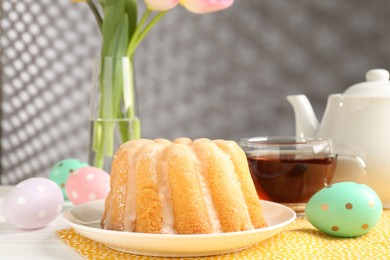 Photo of Delicious bundt cake, Easter eggs and tea on table, closeup