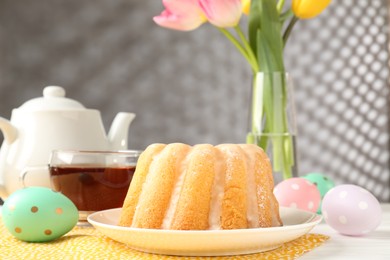 Photo of Delicious bundt cake, Easter eggs and tea on table, closeup