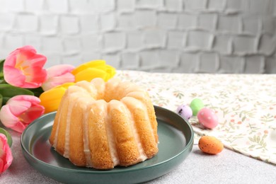 Photo of Delicious bundt cake, Easter eggs and tulips on grey table, closeup