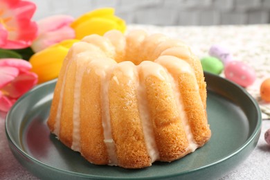 Photo of Delicious bundt cake, Easter eggs and tulips on table, closeup