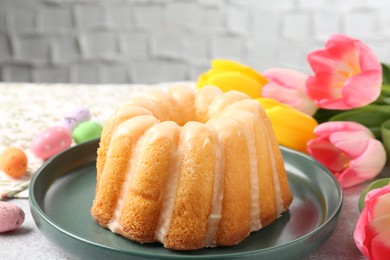 Photo of Delicious bundt cake, Easter eggs and tulips on table, closeup