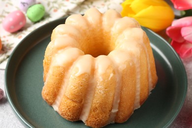 Photo of Delicious bundt cake, Easter eggs and tulips on table, closeup