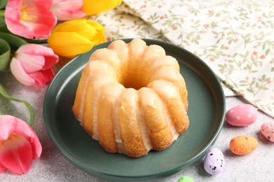 Photo of Delicious bundt cake, Easter eggs and tulips on grey table, closeup