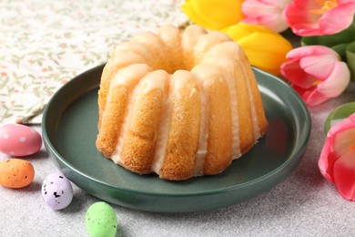 Photo of Delicious bundt cake, Easter eggs and tulips on grey table, closeup