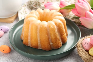 Photo of Delicious bundt cake, Easter eggs and tulips on grey table, closeup