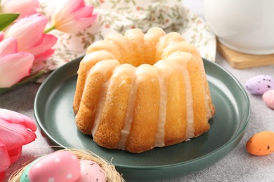 Photo of Delicious bundt cake, Easter eggs and tulips on grey table, closeup