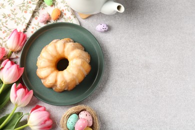 Photo of Delicious bundt cake, Easter eggs and tulips on grey table, flat lay. Space for text