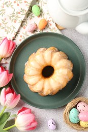 Photo of Delicious bundt cake, Easter eggs and tulips on grey table, flat lay