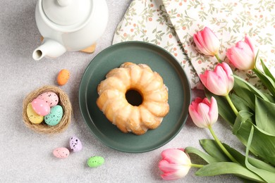 Photo of Delicious bundt cake, Easter eggs and tulips on grey table, flat lay