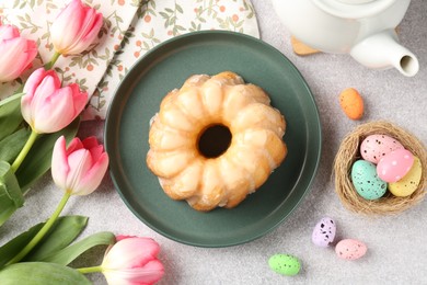 Photo of Delicious bundt cake, Easter eggs and tulips on grey table, flat lay