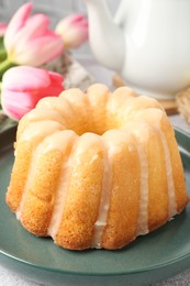 Photo of Delicious Easter bundt cake and tulips on table, closeup