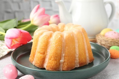 Photo of Delicious bundt cake, Easter eggs and tulips on grey table, closeup