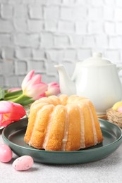 Photo of Delicious bundt cake, Easter eggs and tulips on grey table, closeup