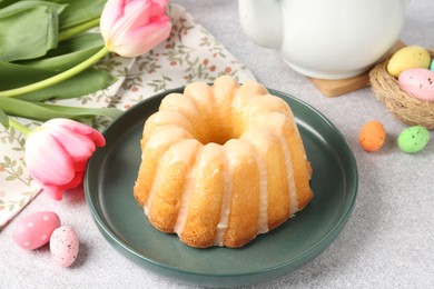 Photo of Delicious bundt cake, Easter eggs and tulips on grey table, closeup