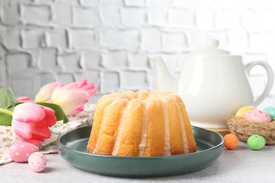 Photo of Delicious bundt cake, Easter eggs and tulips on grey table, closeup