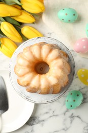 Photo of Delicious bundt cake, Easter eggs and tulips on white marble table, flat lay