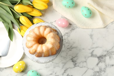 Photo of Delicious bundt cake, Easter eggs and tulips on white marble table, flat lay. Space for text