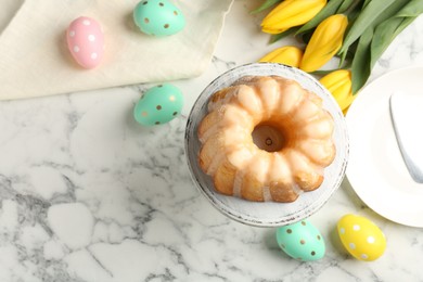 Photo of Delicious bundt cake, Easter eggs and tulips on white marble table, flat lay. Space for text