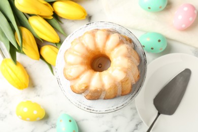 Photo of Delicious bundt cake, Easter eggs and tulips on white marble table, flat lay