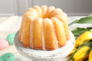 Photo of Delicious bundt cake, Easter eggs and tulips on table, closeup