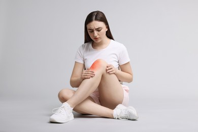 Image of Young woman suffering from pain in knee on light grey background