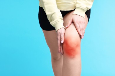 Image of Young woman suffering from pain in knee on light blue background, closeup