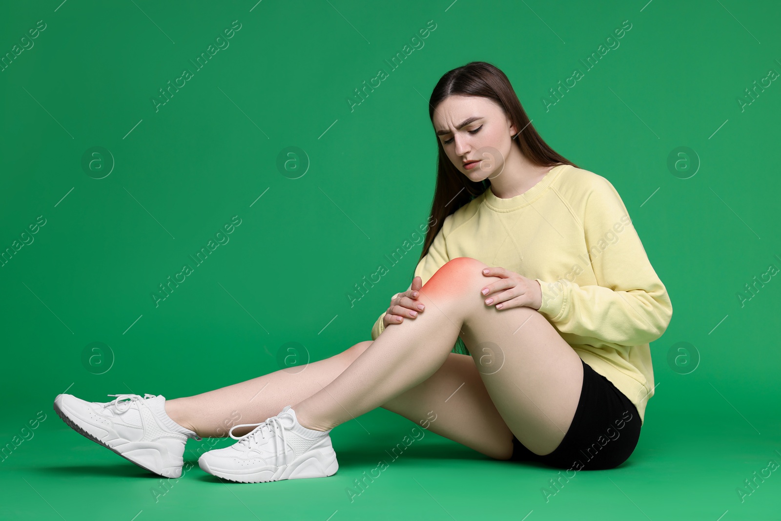 Image of Young woman suffering from pain in knee on green background