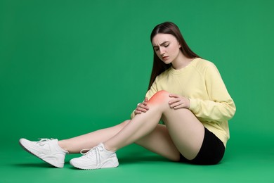 Young woman suffering from pain in knee on green background