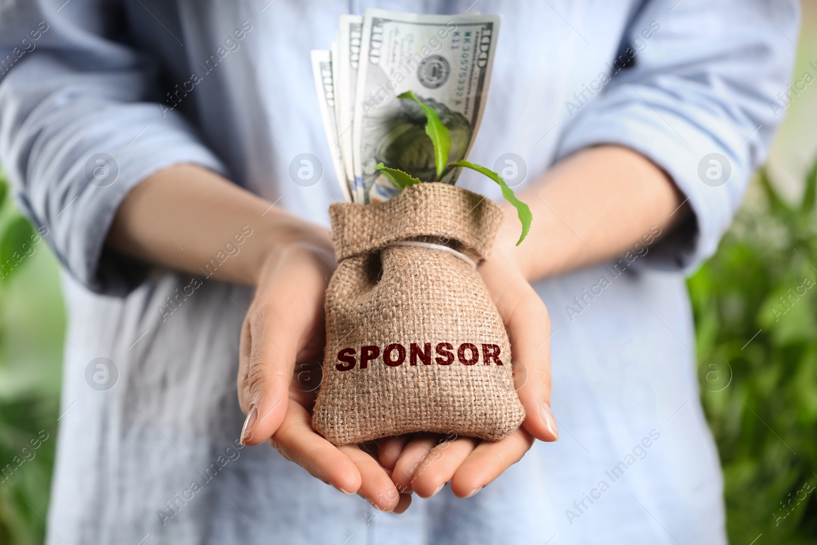 Image of Woman holding sack with dollar banknotes and green sprout on blurred background, closeup. Word Sponsor on bag