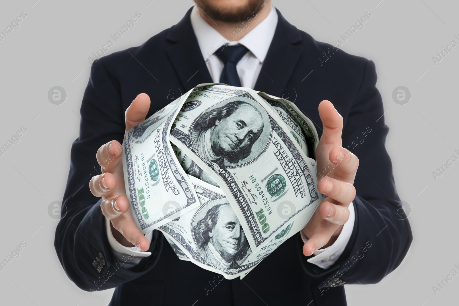 Image of Sponsor. Businessman holding ball of dollar banknotes on light background, closeup