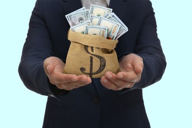 Image of Sponsor. Businessman holding sack with dollar banknotes on light blue background, closeup