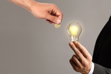 Image of Sponsor offering coin to man with glowing light bulb on grey background, closeup. Sponsorship of idea