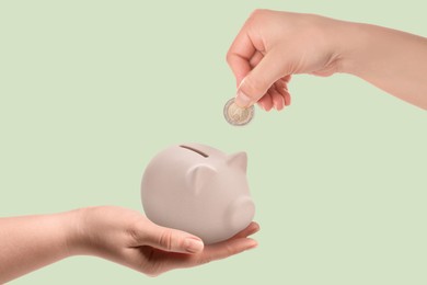 Image of Sponsor offering coin to woman with piggy bank on light green background, closeup