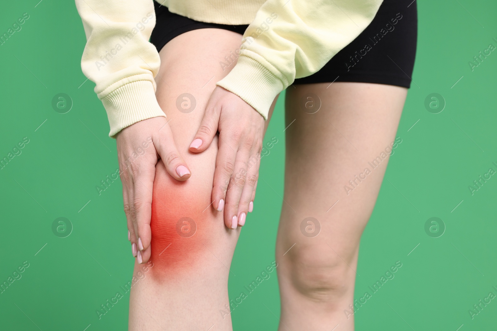 Image of Young woman suffering from pain in knee on green background, closeup