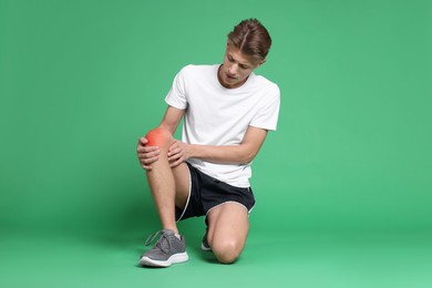 Young man suffering from pain in knee on green background