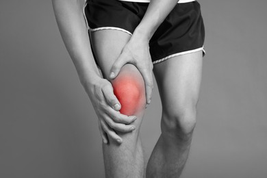 Image of Young man suffering from pain in knee, closeup. Black-and-white effect with red color accent