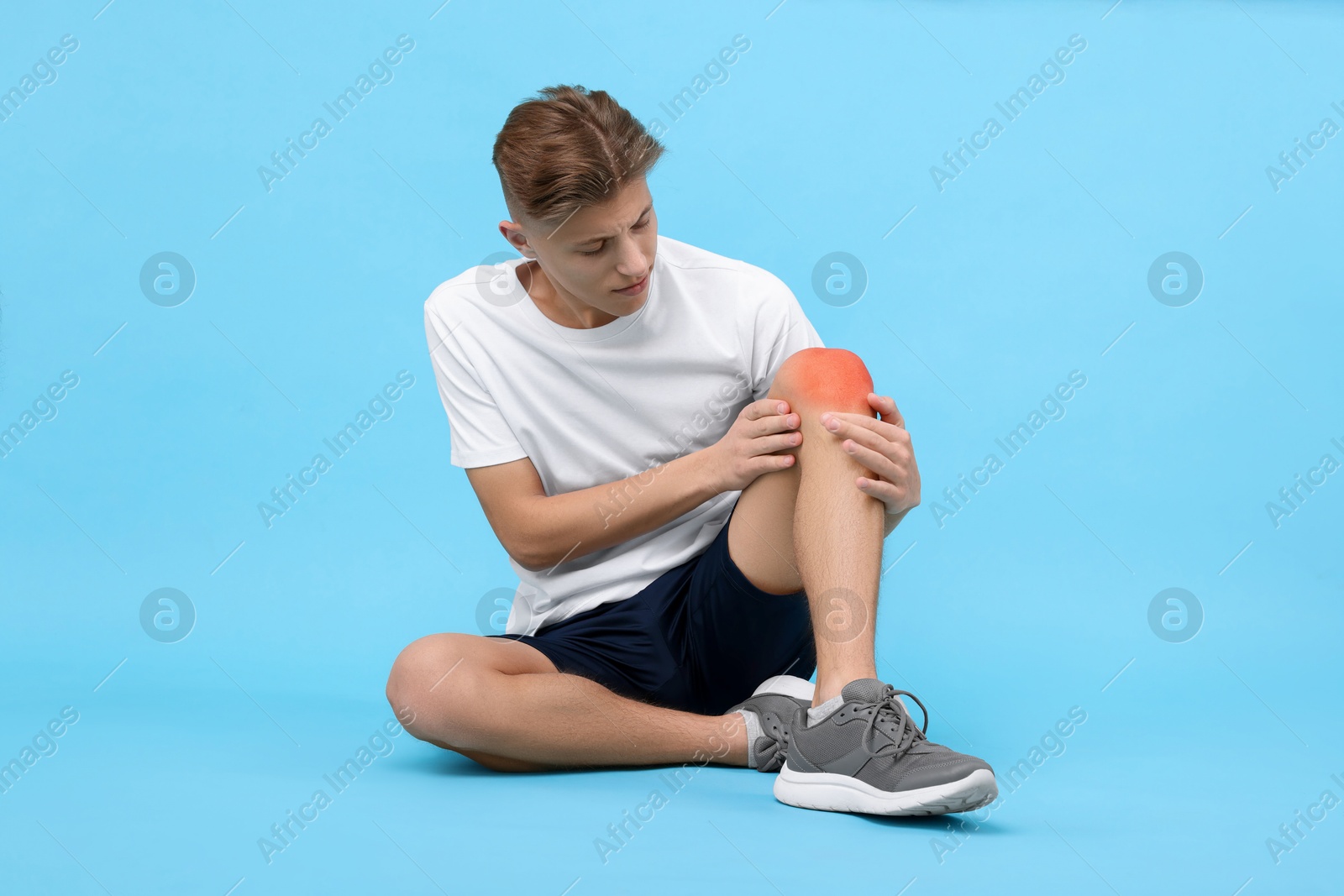 Image of Young man suffering from pain in knee on light blue background