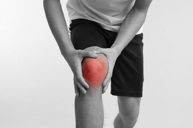 Image of Young man suffering from pain in knee, closeup. Black-and-white effect with red color accent