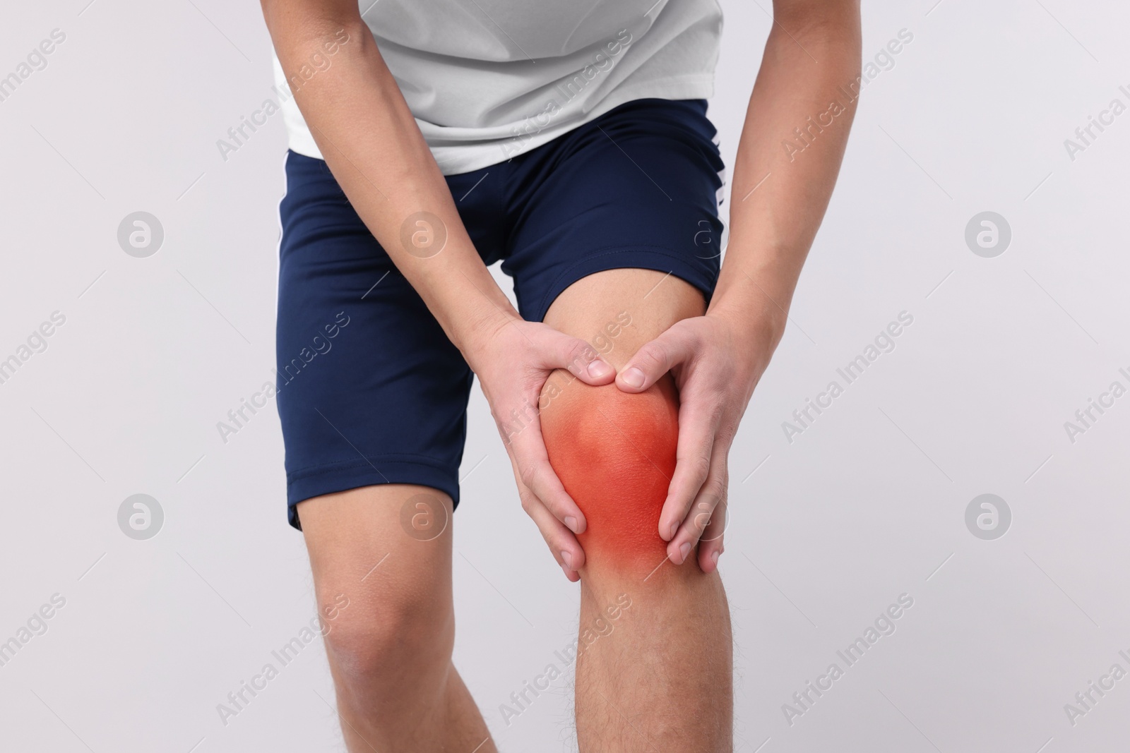 Image of Young man suffering from pain in knee on light background, closeup