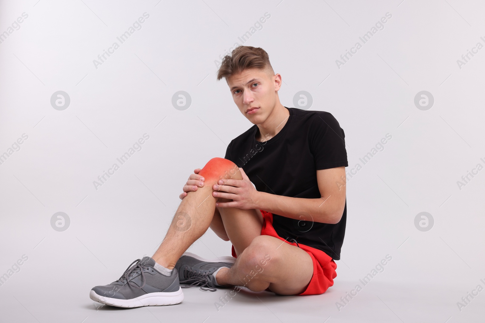 Image of Young man suffering from pain in knee on light background